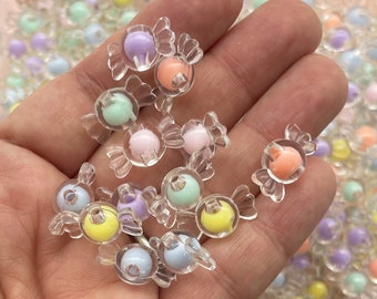 May include: A hand holding a variety of pastel colored candy shaped beads. The beads are clear plastic with a colored center. The beads are approximately 1 cm in diameter.
