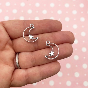 May include: Two silver metal charms shaped like a crescent moon with a star inside. The charms have a loop at the top for attaching to a necklace or bracelet.