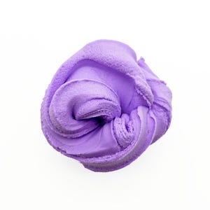 May include: A close-up shot of a swirl of lavender-colored slime against a white background. The slime has a textured appearance, with visible ridges and folds. The color is a soft, pastel purple.