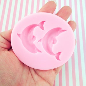 May include: Pink silicone mold with two dolphin shapes. The mold is designed for making fondant or gum paste decorations.