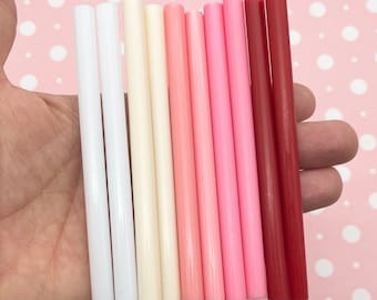 May include: Assortment of ten glue sticks in various shades of pink, white, and red. The glue sticks are arranged in a gradient from white to red.