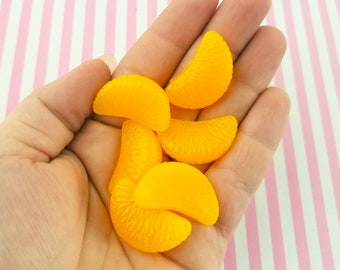 May include: A hand holding six bright yellow orange slices. The slices are arranged in a semi-circle shape, with the tips of the slices pointing towards the center of the hand.