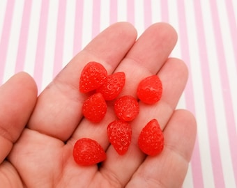 May include: A hand holding a group of small, red, strawberry-shaped resin beads. The beads are glossy and have a realistic appearance.