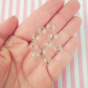 May include: A hand holding a group of clear glass beads. The beads are round and have a smooth surface.
