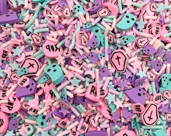 Könnte beinhalten: Nahaufnahme einer Vielzahl von bunten Streuseln, darunter rosa, lila, blau und weiß. Die Streusel haben die Form von Sternen, Kreuzen, Särgen und anderen gruseligen Formen. Die Streusel sind perfekt zum Dekorieren von Kuchen, Cupcakes und anderen Desserts.