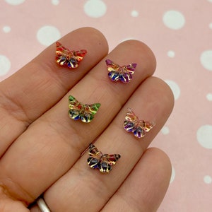 May include: Five iridescent butterfly shaped resin embellishments in various colors, including red, green, blue, purple, and orange. The butterflies are on a hand with a silver ring.