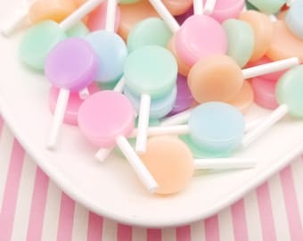 May include: A white plate filled with pastel-coloured lollipop sweets. The lollipops are arranged in a random pattern and have white sticks.