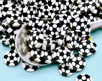 Può includere: Un grande mucchio di zuccherini neri e bianchi a forma di pallone da calcio. Gli zuccherini sono sparsi su una superficie blu e un cucchiaio d'argento ne tiene alcuni.