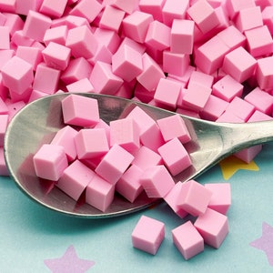 May include: A silver spoon filled with pink sugar cubes. The spoon is on a light blue surface with purple and yellow stars.