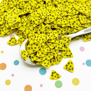 Puede incluir: Un montón grande de amuletos de resina amarillos en forma de triángulo con manchas marrones. Los amuletos están esparcidos sobre una superficie blanca con puntos de colores.