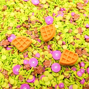 Könnte beinhalten: Nahaufnahme einer Vielzahl von bunten Streuseln, darunter grün, gelb, braun und rosa. Es gibt auch drei orangefarbene Waffelstreusel.