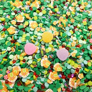 Könnte beinhalten: Eine lebendige Mischung aus dekorativen Streuseln und Süßigkeiten. Der Mix enthält grüne Blattformen, orangefarbene Lebkuchenhaus-Designs und bunte runde Streusel. Drei große, strukturierte Süßigkeiten in Gelb, Rosa und Lila sorgen für einen Farbtupfer.