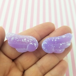 May include: Two lavender-colored resin wing charms with glitter accents. These small, decorative wings are ideal for crafting projects, jewelry making, or adding a whimsical touch to accessories. Each wing is approximately 1 inch in length.