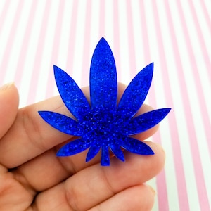 May include: A blue glitter cannabis leaf cutout. The leaf is a popular symbol of the marijuana plant.