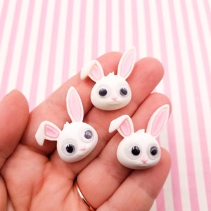 Op de afbeelding: Drie witte konijnencharms met roze oren en grote zwarte ogen. De charms zijn gemaakt van polymer clay en zijn ongeveer 2,5 cm groot.
