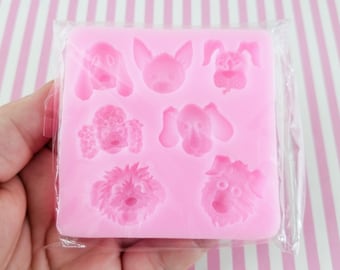 May include: A pink silicone mold featuring various dog faces. The mold includes different breeds and styles, perfect for crafting or baking. The mold is packaged in clear plastic, ready for use.