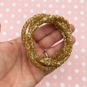 May include: Gold glitter cord, a thick, sparkly cord with a metallic finish. The cord is coiled and appears to be soft and flexible.