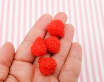 May include: A hand holding five small, red, plastic strawberries.