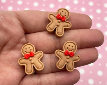 May include: Three gingerbread man figurines with red bow ties. The gingerbread men are brown and have a smiling face.