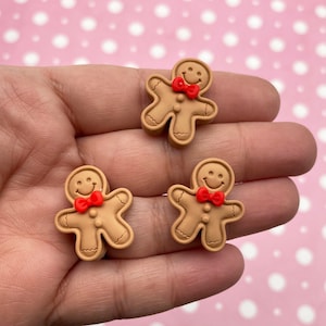 May include: Three gingerbread man figurines with red bow ties. The gingerbread men are brown and have a smiling face.