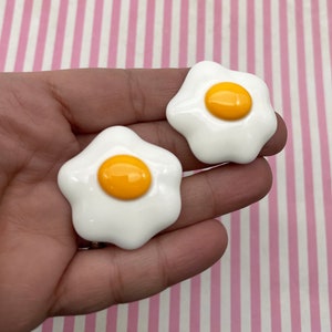 May include: Two white ceramic fried egg shaped charms with yellow centers.