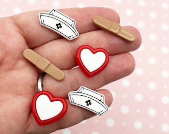 May include: Assortment of six resin flatback cabochons in a variety of shapes and colors. The cabochons include two red hearts, two white nurse hats with a black cross, and two brown bandaids.