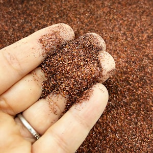 May include: A close-up of a hand holding a pile of fine copper glitter. The glitter is a deep, rich copper color with a slight shimmer.