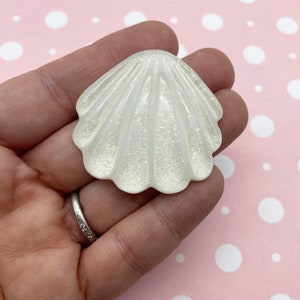 Pode incluir: Uma concha branca iridescente com uma superfície texturizada. A concha é um material artesanal popular para a fabricação de joias, arte de resina e outros projetos criativos.