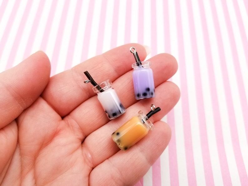 Pu&ograve; includere: Tre ciondoli di bubble tea in miniatura con bevande di diversi colori: viola, bianco e arancione. Ogni ciondolo ha una cannuccia nera e un anello d'argento per appenderlo.