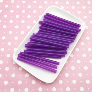 May include: A white plate filled with purple glue sticks. The glue sticks are arranged in a neat stack, with the ends of the sticks facing the viewer.