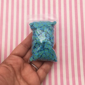 May include: A clear plastic bag filled with small blue and green circle confetti. The confetti is shaped like miniature globes.