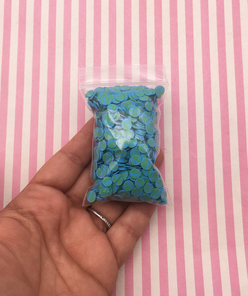 May include: A clear plastic bag filled with small blue and green circle confetti. The confetti is shaped like miniature globes.