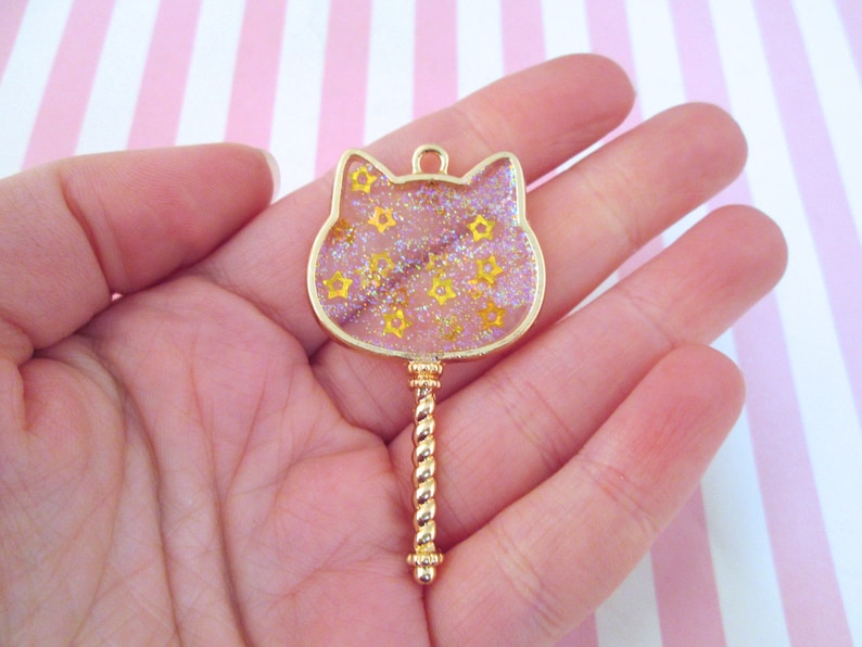 May include: Gold-tone key charm with a clear cat-shaped resin top filled with gold glitter and yellow stars.