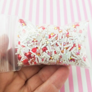 May include: A clear plastic bag filled with red and white sprinkles, including snowflake, star, and round shapes.