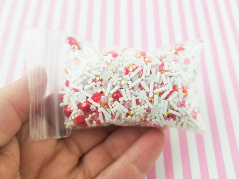 May include: A clear plastic bag filled with red and white sprinkles, including snowflake, star, and round shapes.