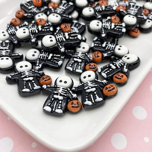 May include: A collection of black and white skeleton figurines holding orange pumpkins. The figurines are made of resin and have a glossy finish.