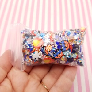Peut inclure: Un sac en plastique transparent rempli de breloques en r&eacute;sine color&eacute;es. Les breloques comprennent des flocons de neige, des cannes en sucre, des &eacute;toiles et d'autres formes sur le th&egrave;me des f&ecirc;tes. Il y a aussi des breloques bleues et orange avec des visages de dessins anim&eacute;s.