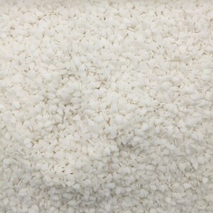 May include: Close-up of a white, granular substance. The image is filled with small, irregularly shaped pieces, creating a textured, almost crystalline appearance. The overall effect is a uniform, bright white surface.
