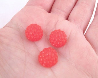 May include: Three red raspberry-shaped candies on a person's hand.