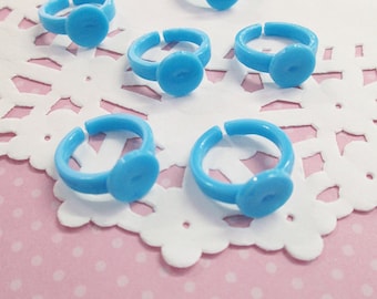 May include: Six light blue plastic rings with a round, flat top. The rings are arranged on a white doily on a pink background.