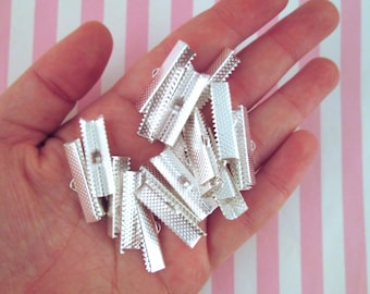 May include: A pile of silver metal clasps for straps or ribbon. The clasps have a textured surface and a small loop on each end.