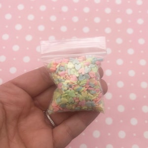 May include: A small clear plastic bag filled with pastel colored heart-shaped sprinkles.