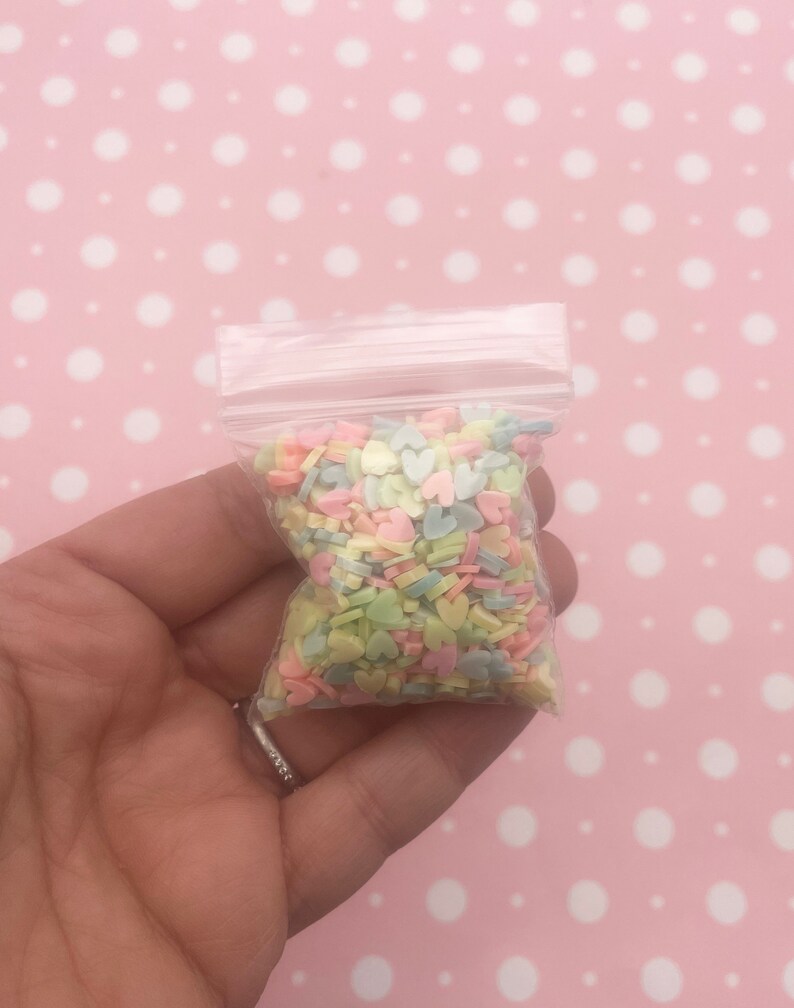 May include: A small clear plastic bag filled with pastel colored heart-shaped sprinkles.