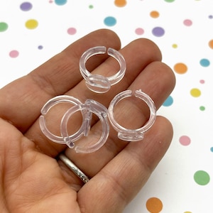 May include: Four clear plastic rings, designed for holding rings or other small items, are shown in a hand.