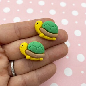 Puede incluir: Dos pequeñas figuritas de tortugas amarillas y verdes. Las tortugas tienen detalles marrones y están hechas de arcilla polimérica.