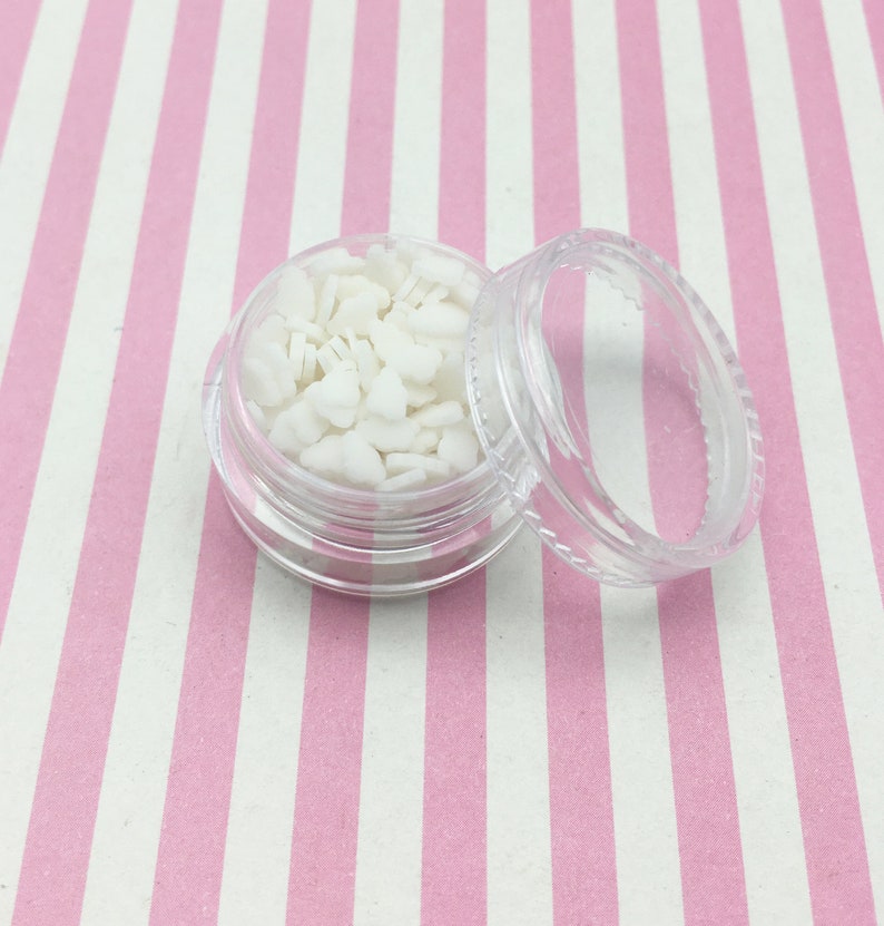 May include: A small, clear plastic jar filled with white bunny-shaped confetti. The jar's lid is off, revealing the contents. The background is a pink and white striped pattern.