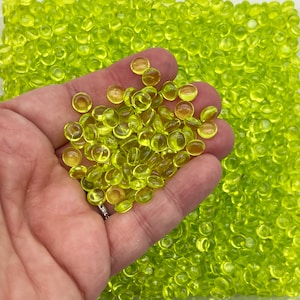 Pu&ograve; includere: Una mano che tiene una grande quantit&agrave; di piccole perline di vetro rotonde, traslucide, di colore verde lime.