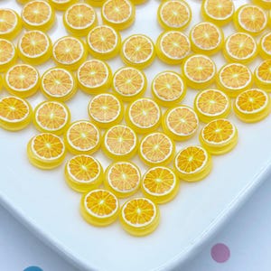 May include: A white plate filled with yellow and orange round resin orange slices. The orange slices have a realistic look and are perfect for crafting.