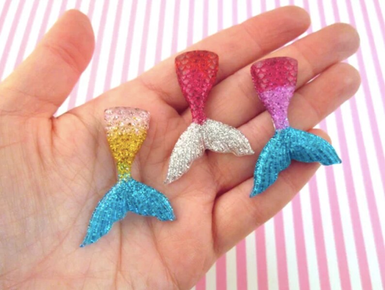 Puede incluir: Tres abalorios de cola de sirena con purpurina en diferentes colores. Las colas est&aacute;n hechas de pl&aacute;stico transparente con purpurina incrustada. Las colas son de color rosa, azul y amarillo.