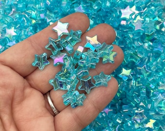 May include: A hand holding a handful of iridescent blue star-shaped beads. The beads are made of glass and have a holographic finish.